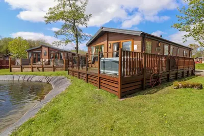 a cabin with a large deck next to a body of water at Coniston in Carnforth
