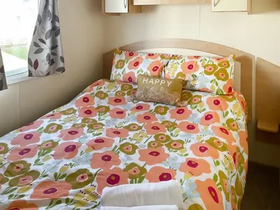 a bed with a floral bedspread and a happy pillow at Sea Breeze in Heysham