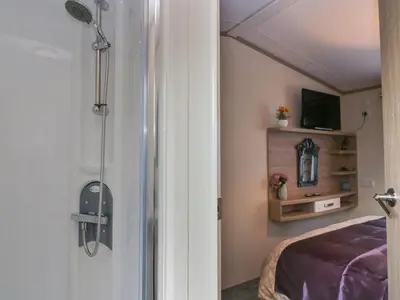 a shower in a room with a bed and a tv at Ladybird Lodge in Carnforth