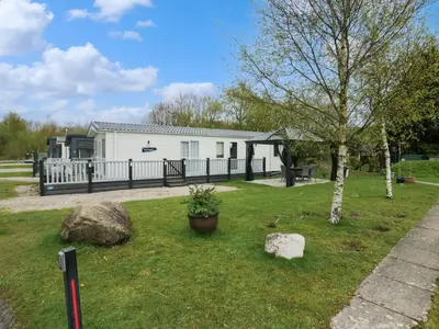 a white house with a fence and a tree at Ladybird Lodge in Carnforth