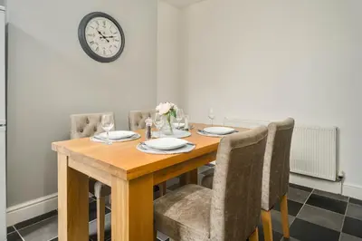 a dining room table with chairs and a clock on the wall at Willow House - 2-Bedroom House In Merseyside! in Birkenhead