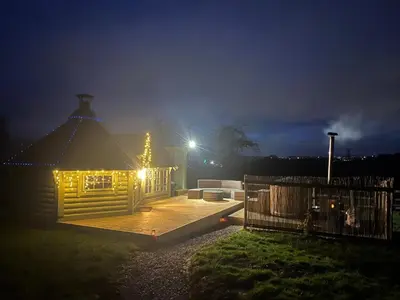 a house with lights on a deck at night at Off GRID Hobbit Hut with Wood Burning Hot tub NO SHOWER in Hapton