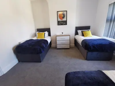 a bedroom with two beds with blue sheets and yellow pillows at Comfy and Cozy 3 Bed house, free parking & Wifi in Birkenhead