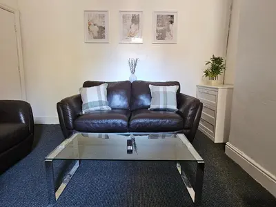 a living room with a leather couch and a glass coffee table at Convenient 3 bed, Pr1 near Uclan n Train station in Preston