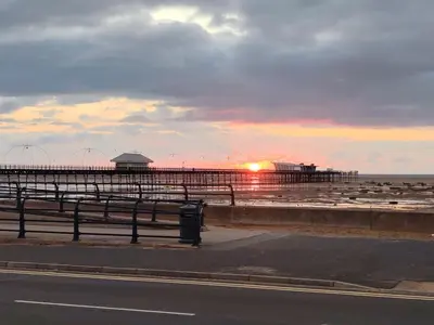 a beach with a pier and the ocean at sunset at Lakeside View in Southport