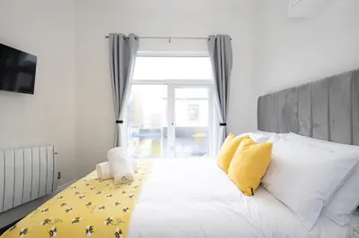 a white bed with yellow pillows and a window at Cozy Boutique Studios Perfect for Contractors & Travelers in Bolton
