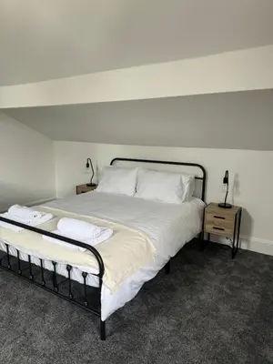 a bedroom with a large bed with white sheets and pillows at The Eaves - Victorian second floor, open plan apartment in Southport