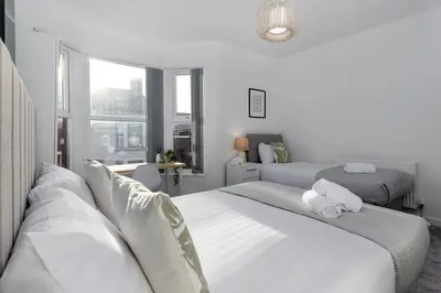 a white bedroom with two beds and a window at Cowley House - Air Host & Stay - Sleeps 7 in Liverpool