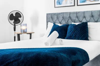 a bed with blue and white sheets and a fan at Anfield Four-Bed Spacious Getaway Haus in Liverpool