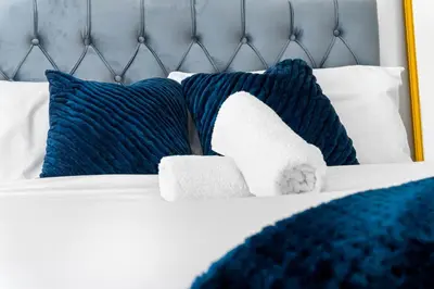 a bed with blue and white pillows on it at Anfield Four-Bed Spacious Getaway Haus in Liverpool