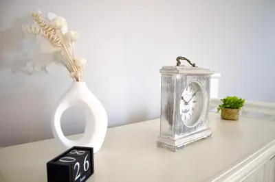 a table with a clock and a vase with flowers at Spacious Flats in St Helens, Merseyside in Saint Helens