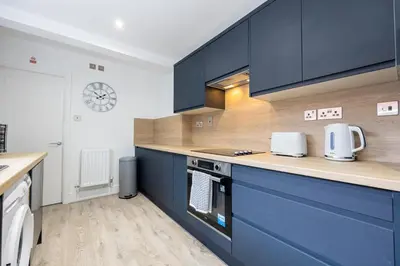 a kitchen with blue cabinets and a clock on the wall at Cozy Modern Home Games Room & Cinema Perfect for 8 in Bolton