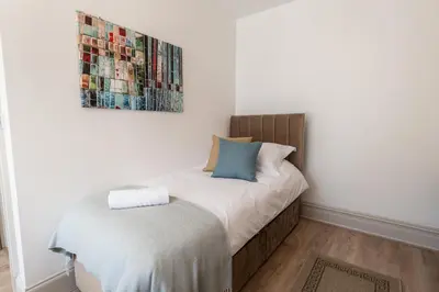 a bed in a room with a painting on the wall at Comfy 5 star Stays - 6 Bedrooms - Sleeps 8 - Free Parking & WiFi - Wirral in New Brighton