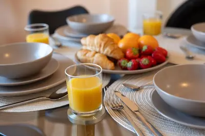 a table with a glass of orange juice and a plate of fruit at Terracotta Apartment, free WiFi & parking, coastal location in New Brighton