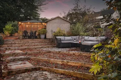 a patio with a couch and a table in a garden at Coronation Family Cottage, Modernised 200-Year-Old Lake District Cottage with Private Hot Tub and Parking - Ridgestone in Lindale