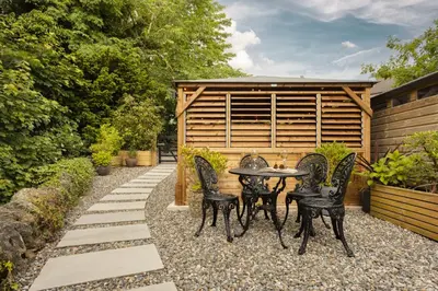 a patio with a table and chairs in a garden at Coronation Family Cottage, Modernised 200-Year-Old Lake District Cottage with Private Hot Tub and Parking - Ridgestone in Lindale