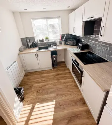 a kitchen with white cabinets and a wooden floor at Stylish Modern Apartment in Blackpool with Parking in Blackpool