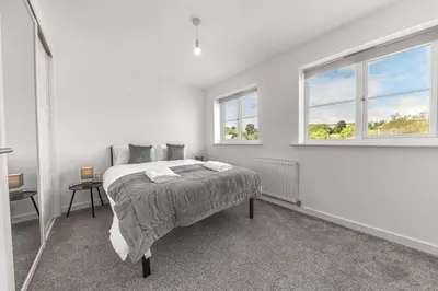 a white bedroom with a bed and two windows at Barrow Central 3 Bedroom House in Roose