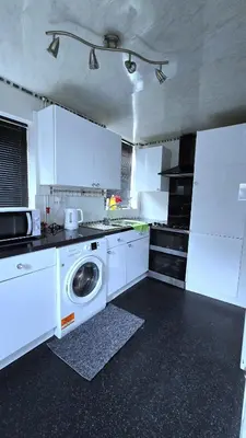 a kitchen with white cabinets and a washing machine at Ritchie Guest House in Wigan