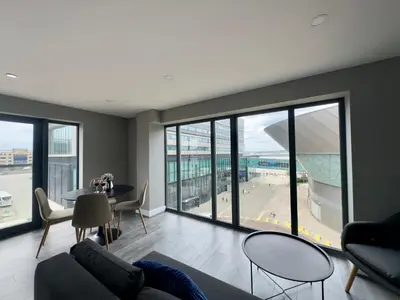 a living room with a table and chairs and windows at Monarchs Quay Arena Apartments by Happy Days in Liverpool