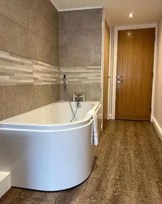 a large white tub in a bathroom with a wooden door at Clock Tower Apartments 1 in Morecambe