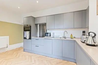 a kitchen with white cabinets and a wooden floor at Stylish House - Sleeps 7 - Free Parking, Fast WiFi and Smart TV - Contractors, Groups and Long Stays Welcome by Yoko Property in Wigan
