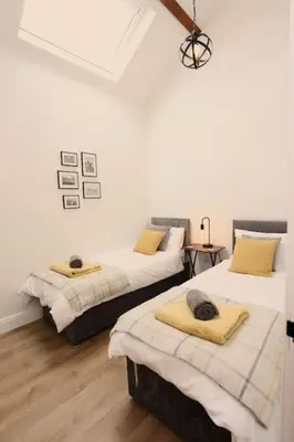 two beds in a room with white walls and wood floors at Stunning Coach House with two bedrooms and parking in Hambleton