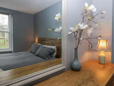 a mirror in a bedroom with a bed and a vase with flowers at Willow Cottage in Carnforth