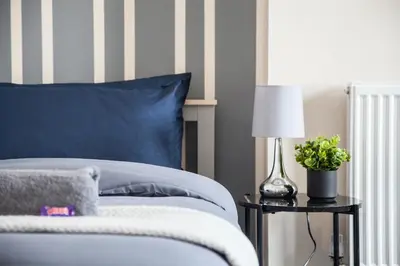 a bed with a blue pillow and a lamp on a table at Spacious House 10min to Liverpool Centre in Wallasey