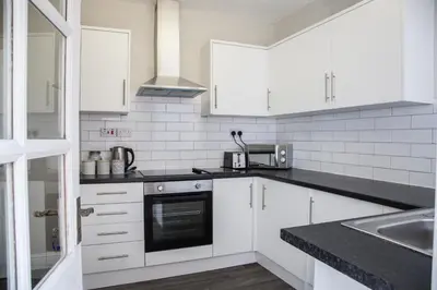 a kitchen with white cabinets and a black counter top at Spacious House 10min to Liverpool Centre in Wallasey