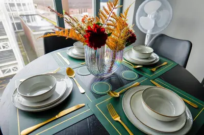 a table with plates and a vase of flowers on it at Waterfront Luxury Apartment in Liverpool