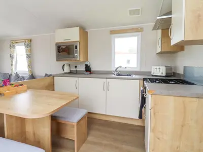 a kitchen with white cabinets and a wooden table at Windermere Lodge in Morecambe