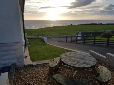 a picnic table and bench next to the ocean at Half Moon Bay in Heysham