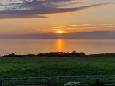 a sunset over the ocean with a green field at Half Moon Bay in Heysham