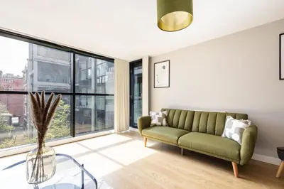 a living room with a green couch and large windows at Host & Stay - The Pall Mall Apartment in Liverpool