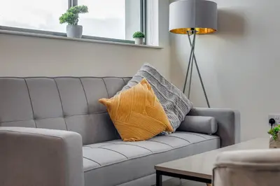 a gray couch with an orange pillow in a living room at Huge Long Stay Savings! City View Balcony Penthouse in Liverpool