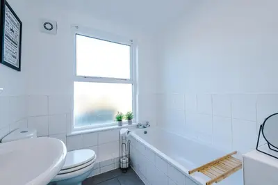 a white bathroom with a tub and a toilet and a window at Private garden maisonette near city centre! Walking distance from Anfield in Liverpool