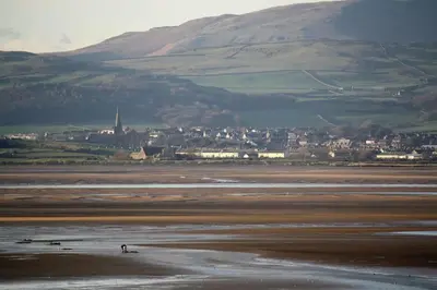 a person riding a horse on a beach with a city in the background at The Rafters Bank House Stunning Apartment in Millom