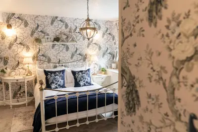 a bedroom with floral wallpaper and a bed with blue and white pillows at Peacock Room at Field View Cottage in Eccleston