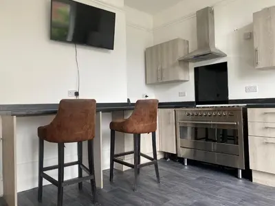 a kitchen with two bar stools and a tv at Springfield Guesthouse in Blackburn