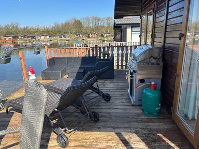 a deck with a table and a stroller and a grill at Gressingham 9 - South Lakes Leisure Village - lodge on the lake in Carnforth