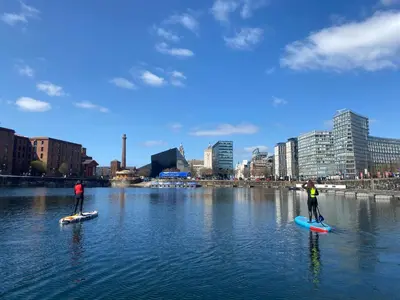 two people are standing on paddle boards in the water at Chapel Apartment in Liverpool