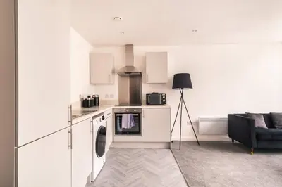 a white kitchen with a stove top oven next to a couch at Central Preston Lovely 1 Bedroom Apartment in Preston