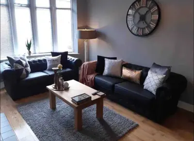 a living room with couches and a table and a clock at Seaside Suites in Blackpool