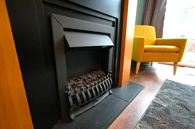 a fireplace in a living room with a yellow chair at Detached Homestay - Super, King & Double Rooms - Leyland, Preston, Chorley, Lancashire in Leyland