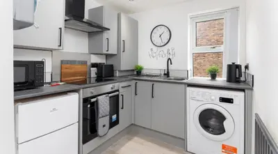 a kitchen with white cabinets and a washer and dryer at Residency apartments Sefton road in Walton on the Hill