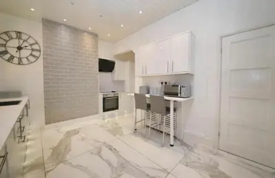 a kitchen with white cabinets and a clock on the wall at 3 BR- Central Wigan- HOT TUB in Ince-in-Makerfield