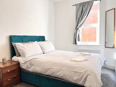 a bedroom with a bed with a blue headboard and a window at Apartment 6 in Blackpool