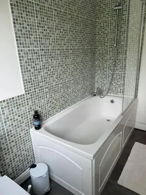 a white bath tub in a tiled bathroom at Sunshine cottage in Horwich