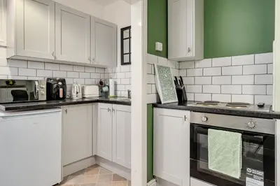 a kitchen with white cabinets and green accents at The Old Bike Cabin Flat 1 in Heapey